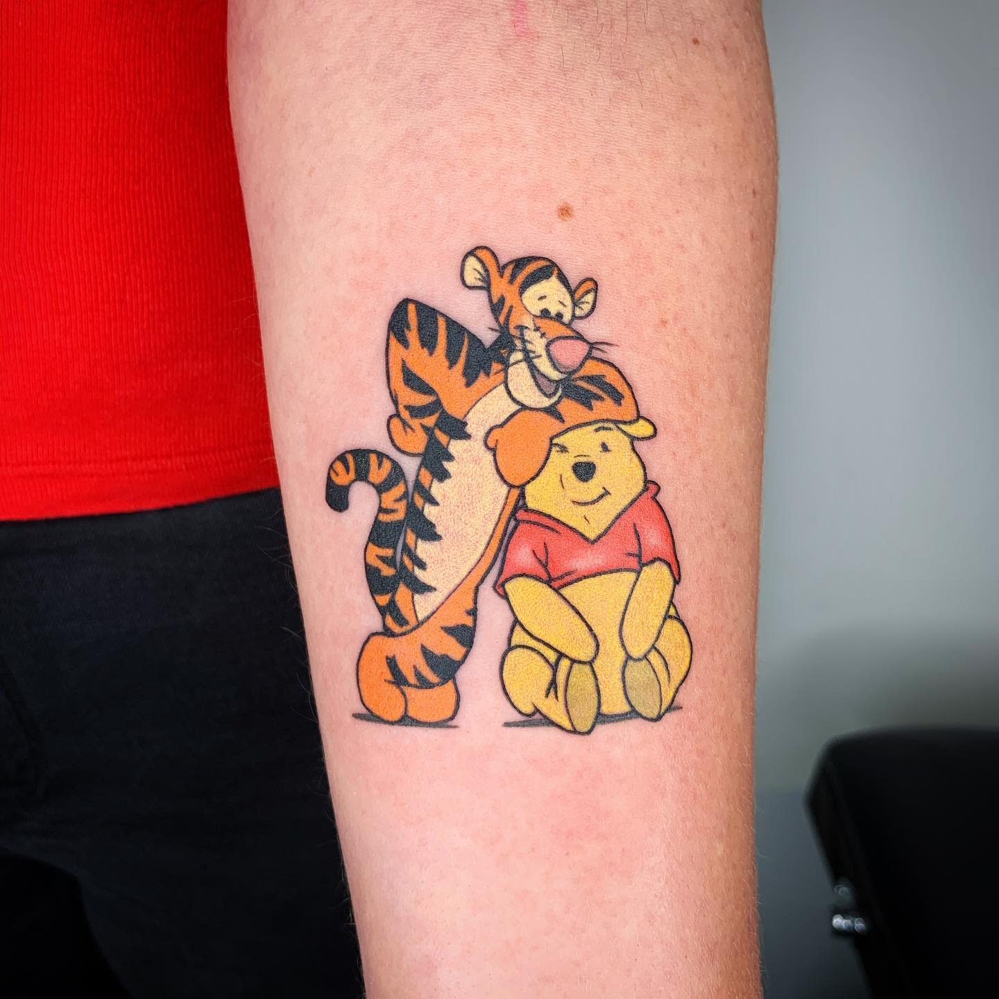 Tattoo of Tigger and Winnie the Pooh hugging, with Pooh wearing a red shirt